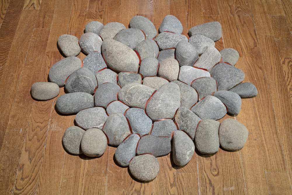 installation image of Smoulder, a round pile of stones placed directly on the floor with inlaid copper that gives the impression that the contact points of the stone are glowing hot.