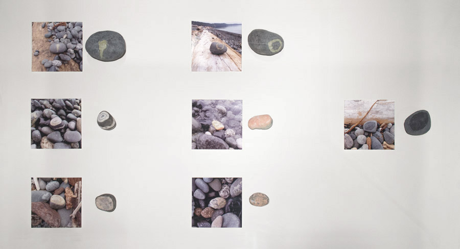 seven ceramic stones in a vitrine next to photos of their döpplegangers on a beach