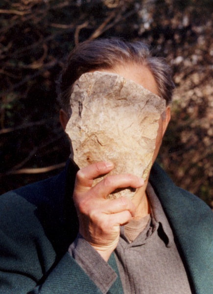 A man (the artist, Jimmie Durham) is holding a stone in front of his face, almost a perfect mirror of the shape of his head, it completely obscures his face.